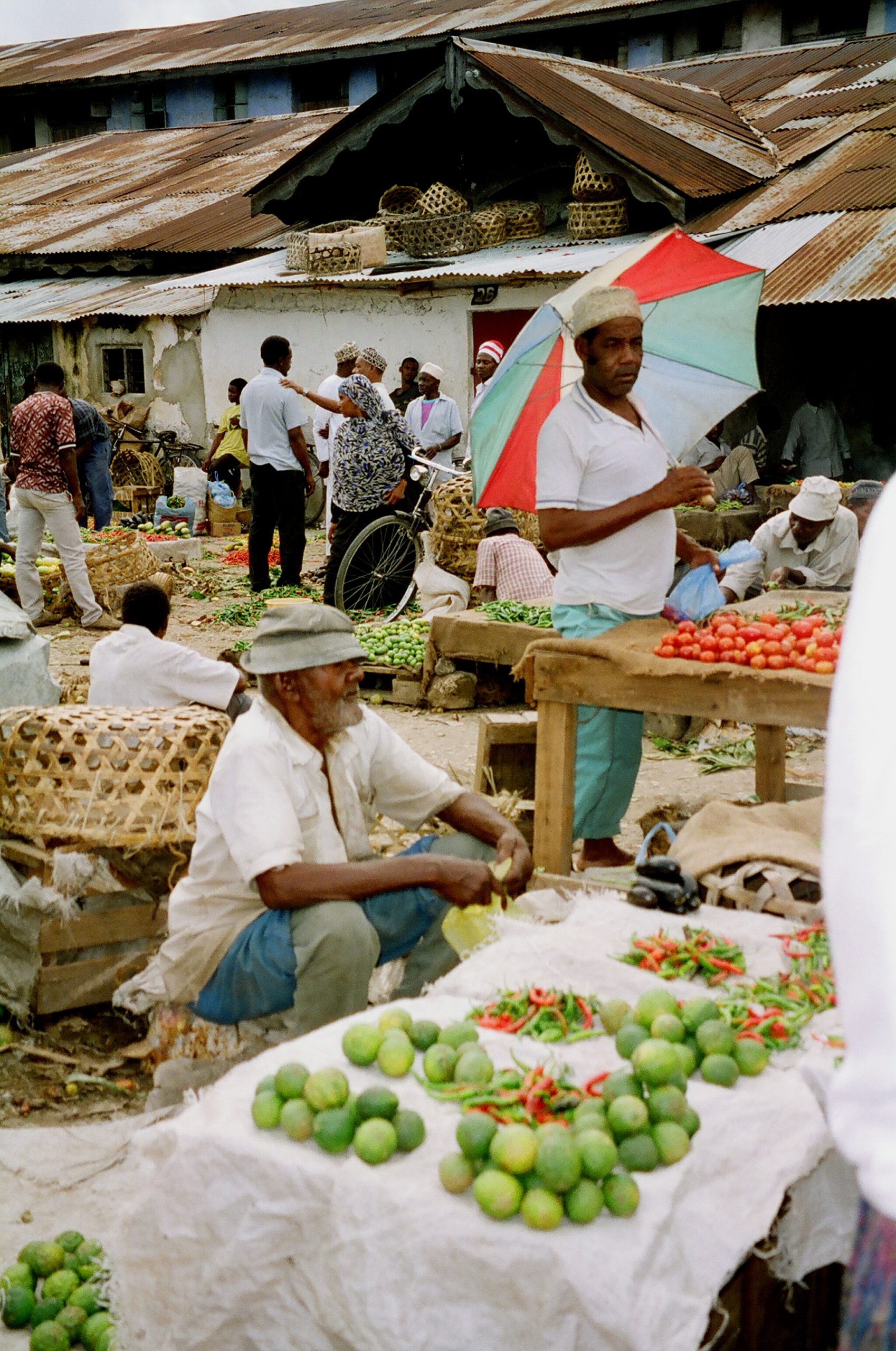 Chilli — Men selling pili pili (chili peppers) and tomatoes at an outdoor market in Zanzibar, Tanzania, photographed 1997. Genuine Tanzania-specific chili commerce photograph (market/vendor scene rather than a farm-growing shot) — the only open-licensed, Tanzania-provenanced chili photograph located in this research pass.