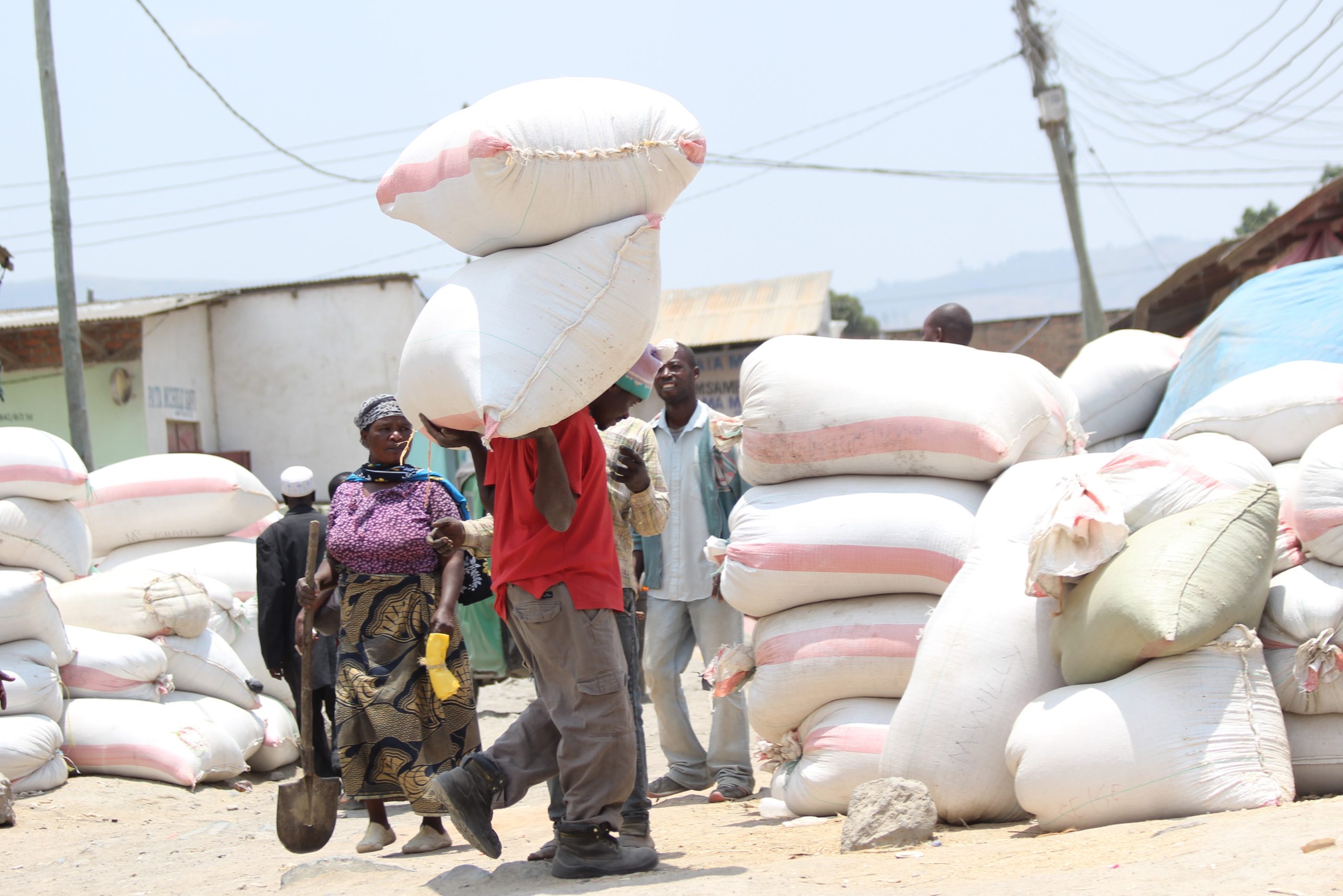 Man carrying sacks of rice past stacks of bagged rice at a market, Tanzania